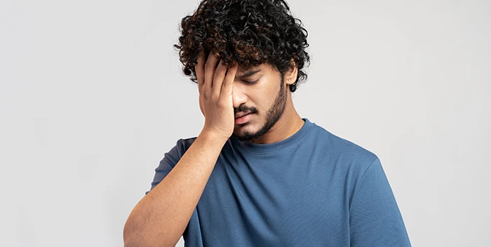 Un hombre de pelo rizado cubriéndose la cabeza con la mano.