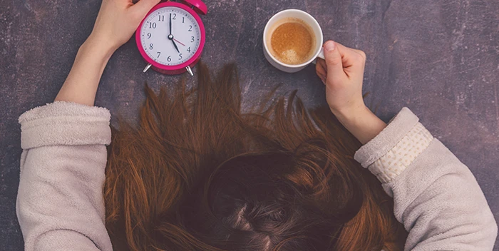 Una mujer acostada con una taza de café y un despertador.