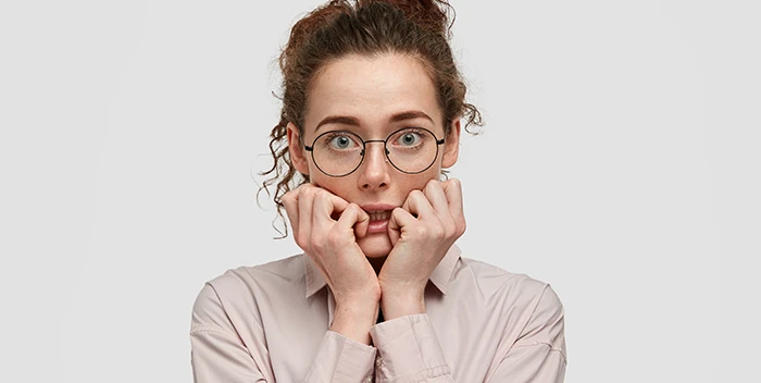 Una mujer con gafas cubriéndose la cara con las manos.