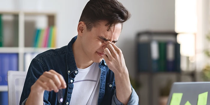 Un hombre está sentado frente a una computadora portátil con los ojos cerrados.