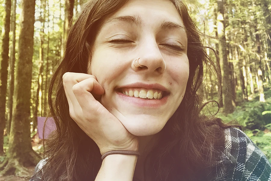 Una mujer joven sonriendo en el bosque, que no se ve afectada por la dificultad para respirar provocada por la ansiedad.