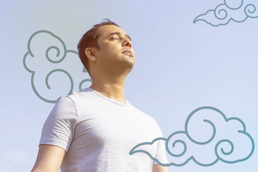 Un hombre está parado frente a un cielo azul con nubes al fondo, sintiendo ansiedad y dificultad para respirar.