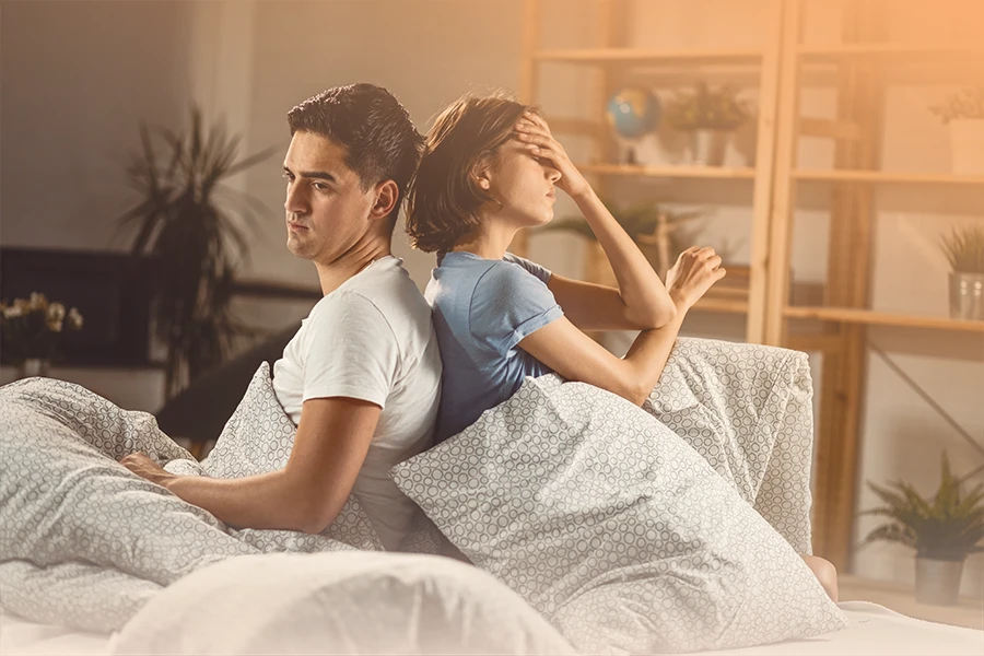 Una pareja que experimenta ansiedad en su relación se sientan juntas en la cama de una habitación.
