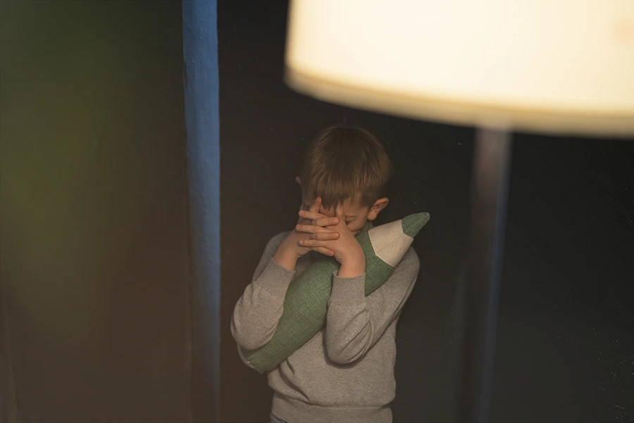 Se representa a un niño que experimenta una experiencia infantil sosteniendo una almohada frente a una lámpara, lo que simboliza su búsqueda de un tratamiento para la ansiedad infantil.