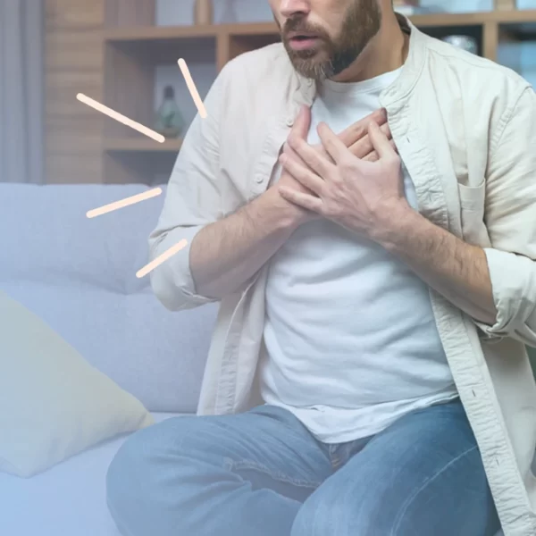 Un hombre está sentado en un sofá, visiblemente luchando contra la ansiedad mientras se agarra el pecho.