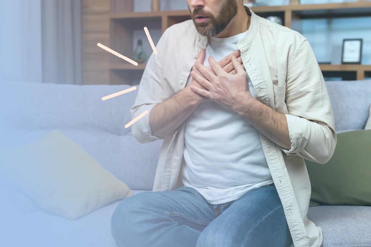 Un hombre está sentado en un sofá, visiblemente luchando contra la ansiedad mientras se agarra el pecho.