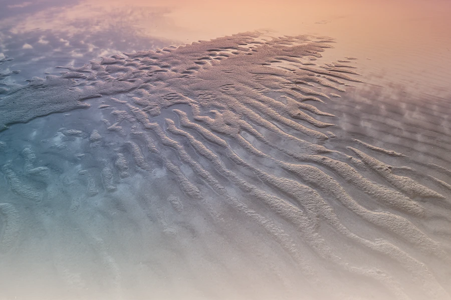 Vista aérea de una playa de arena con patrones ondulados al atardecer, que ofrece un entorno sereno que podría ayudar a curar la ansiedad generalizada.