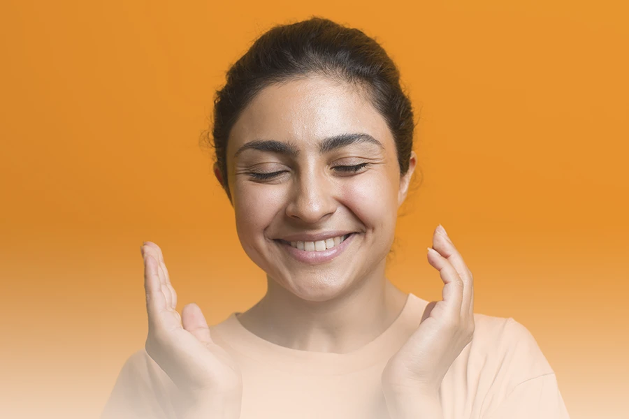 Una mujer sonriente con los ojos cerrados toca suavemente su cara, experimentando parestesia por ansiedad mejor conocida como hormigueo cuerpo por ansiedad.