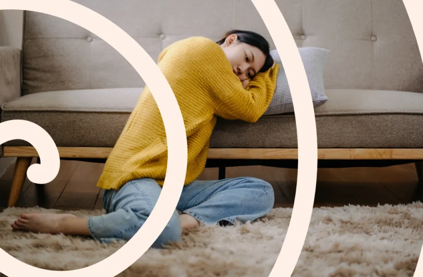 Una persona con un suéter amarillo y jeans está sentada sobre una alfombra mullida, apoyada en el sofá con la cabeza apoyada en una almohada, absorta en sus pensamientos. Un patrón de remolinos blancos se superpone a la imagen, capturando sutilmente su ansiedad psíquica.