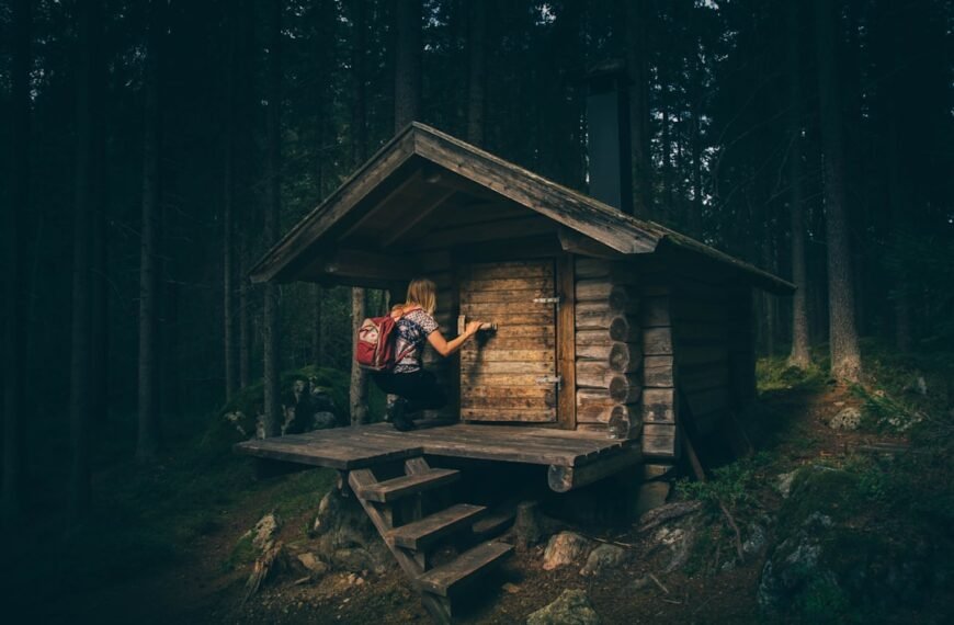 Con ansiedad y ganas de vomitar, una persona con mochila abre la puerta de una pequeña cabaña de madera en el denso bosque.