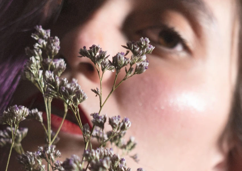 Un primer plano del rostro de una persona con una flor, captando un momento sereno que invita a reflexionar y mejora tu autoestima.