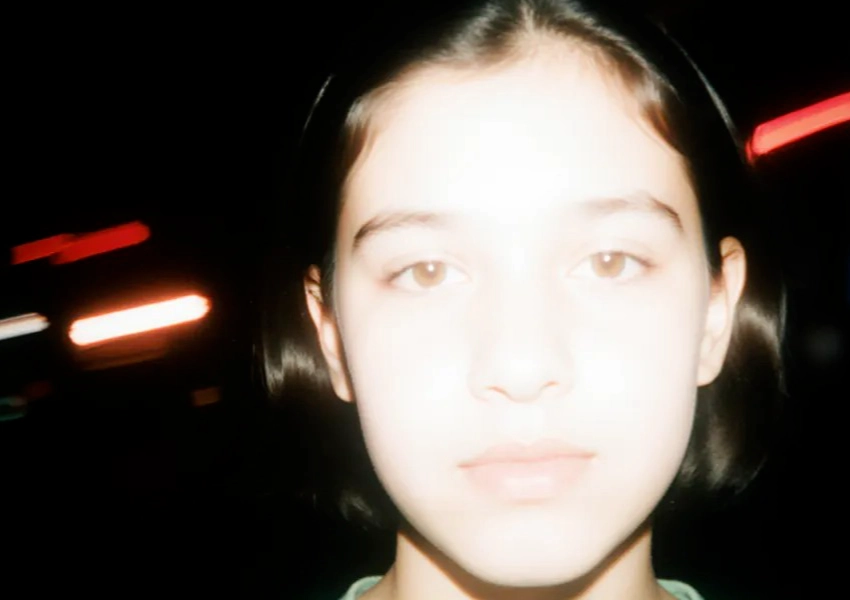 Primer plano de una persona joven con pelo corto y oscuro, expresión neutra y rostro iluminado sobre un fondo oscuro con luces difuminadas, que capta los sutiles matices de la autoestima en adolescentes de secundaria.